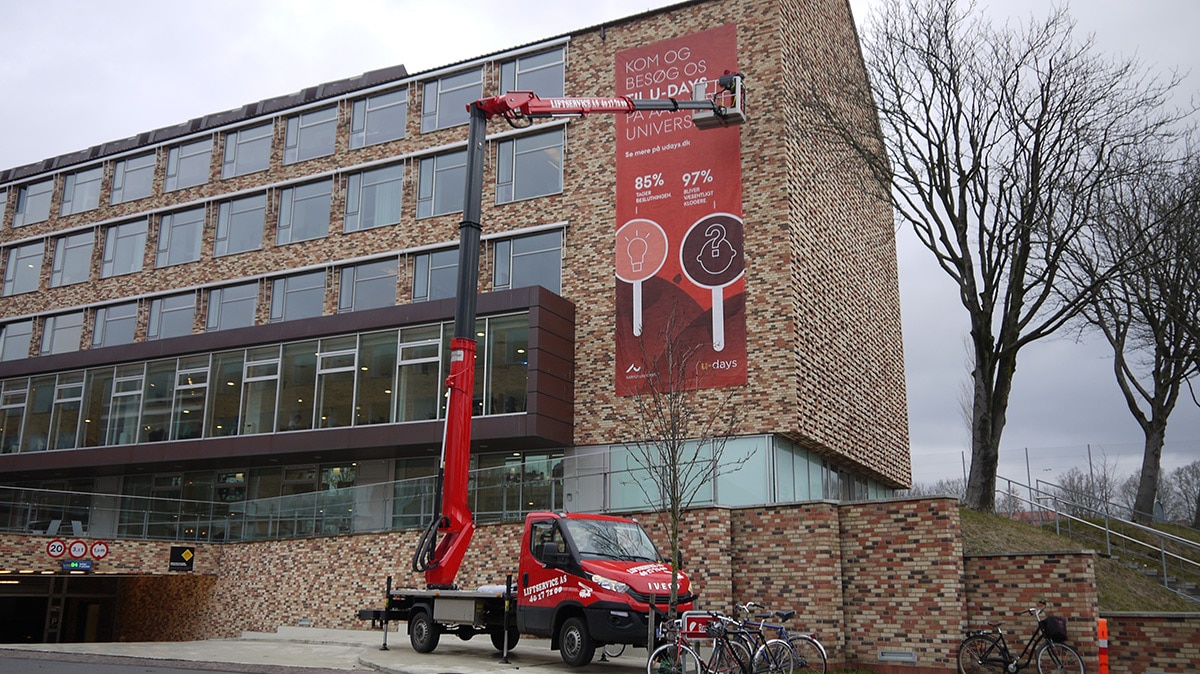 Liftservice monterer stort rødt banner på universitetsbygning